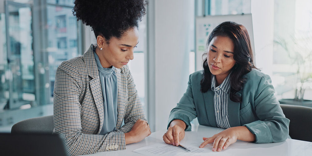 Two professionally dressed women reviewing a document in an office.