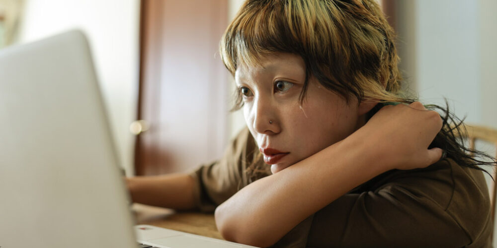 Woman sitting at a desk, leaning forward, looking at a computer screen.