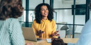 Happy woman in an office setting sitting at a table speaking to colleagues